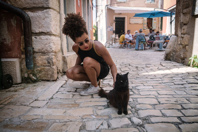 Young woman stroking stray cat on cobbled footpath in town