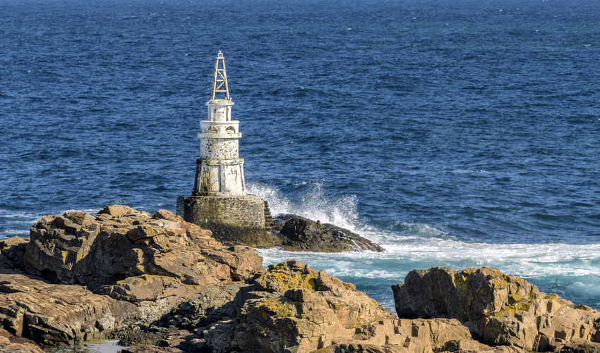 Lighthouse on rock by sea against buildings