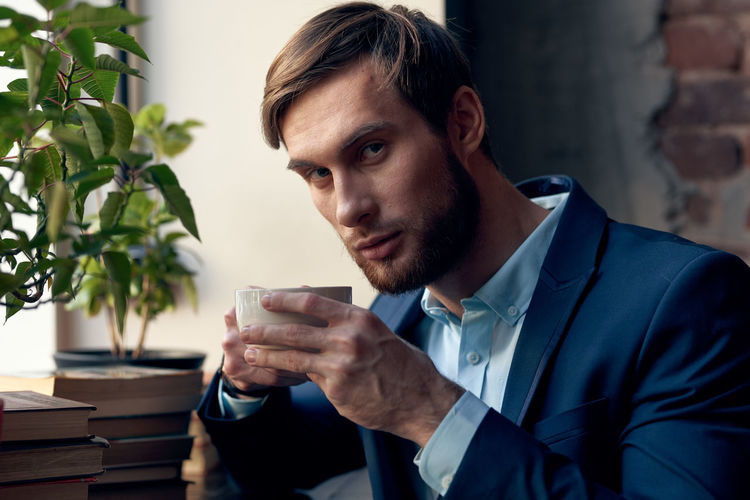 Portrait of young man holding coffee cup at table