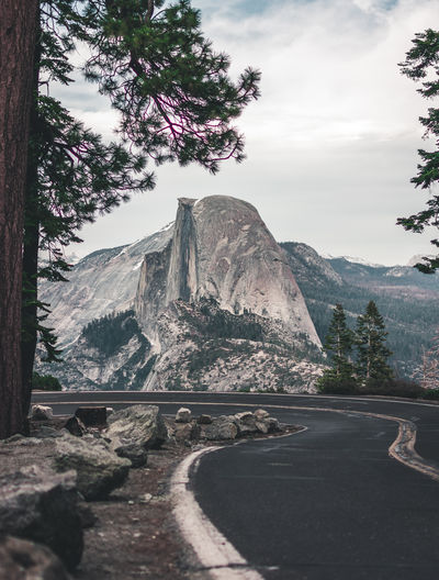 Road amidst trees and mountains against sky