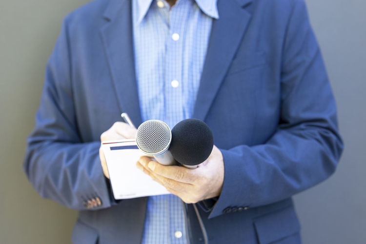 Reporter at media event or news conference, holding microphone, writing notes. broadcast journalism.