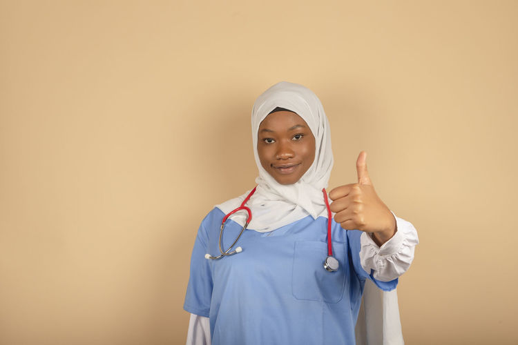 African american nurse with headscarf showing thumb up, posing on light background, free space