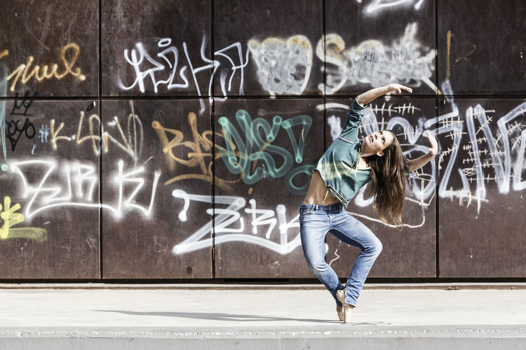 Full length of woman dancing against graffiti on wall