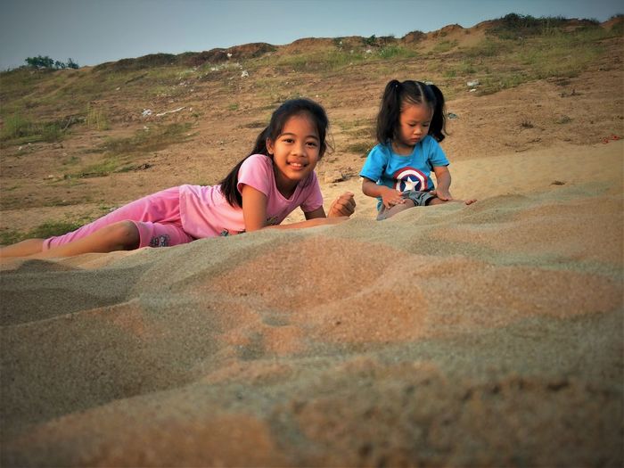 Portrait of girl with sister reclining on sand at beach