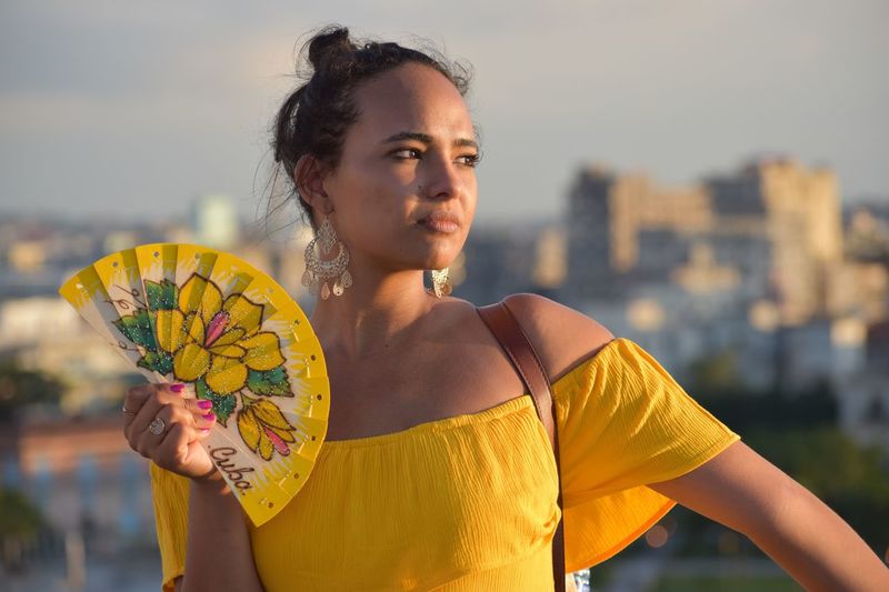 Woman with hand fan standing against sky in city