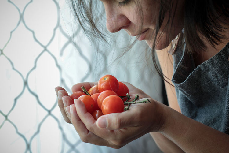 Woman smelling fresh cherry tomatoes against window 