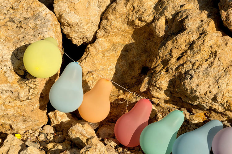 High angle view of colorful balloons tied with rope on rock during sunny day