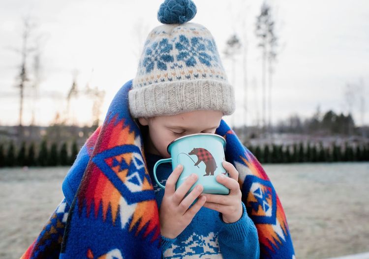 Young boy wrapped in a blanket drinking hot chocolate outside