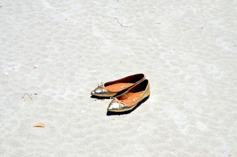 High angle view of flat shoes at sandy beach on sunny day
