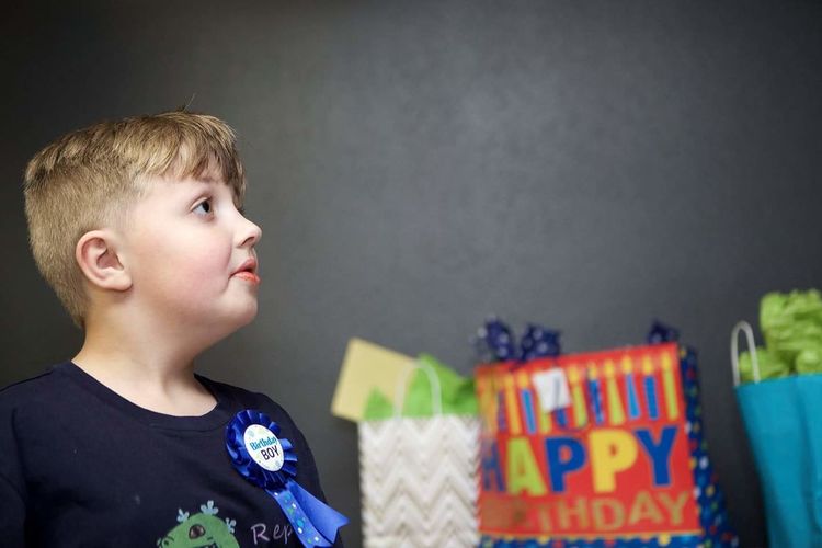 Boy looking away with birthday gifts against black wall in background