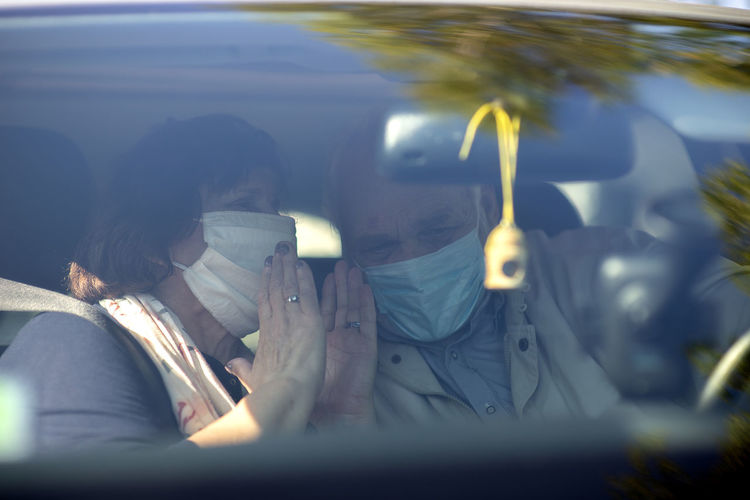 Happy senior couple wearing anti virus masks are driving in a car during the covid-19 pandemic