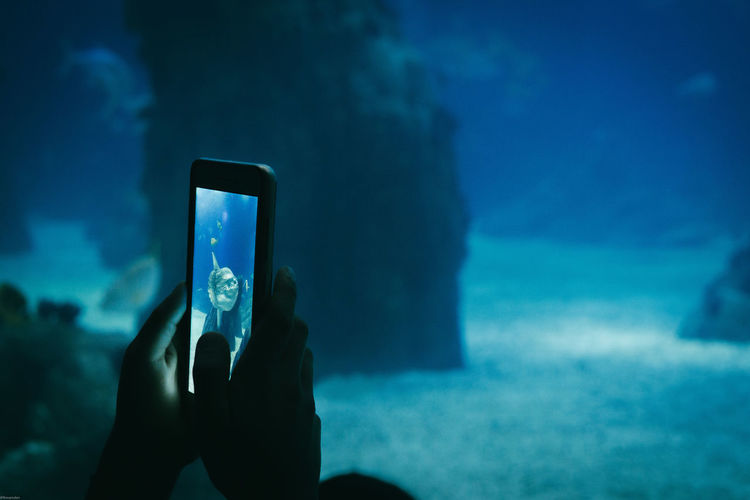 Close-up of hand holding smart phone against blue sea
