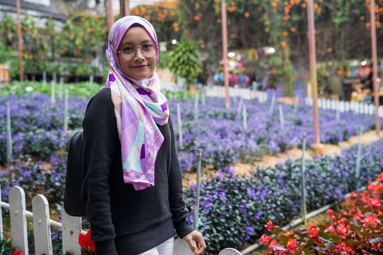 Portrait of a smiling young woman standing on purple flowering plants