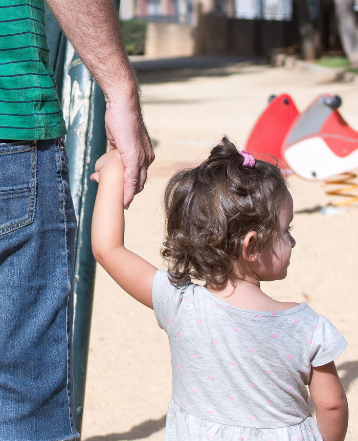 Midsection of father holding hand on daughter in park