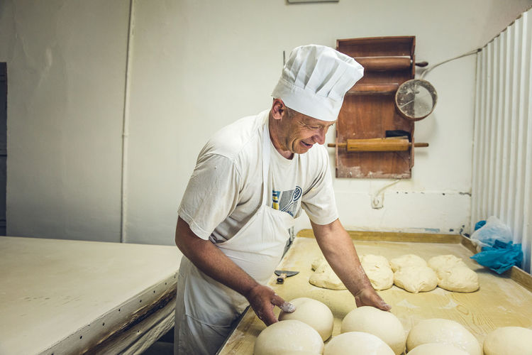 Smiling man arranging dough at a bakery in belgrade, serbia