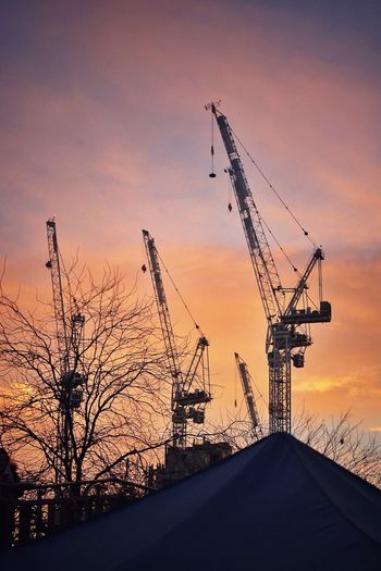 Silhouette cranes against sky during sunset