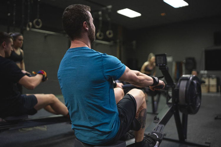 Man using rowing machine with people exercising in background at gym
