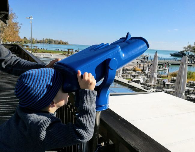 Boy using binoculars against blue sky