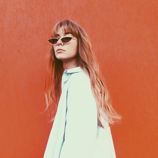 Portrait of young woman wearing sunglasses by against red wall