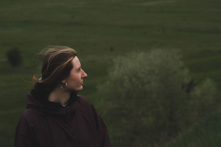 Woman in a rain anorak stands on the hill, deep green background. 