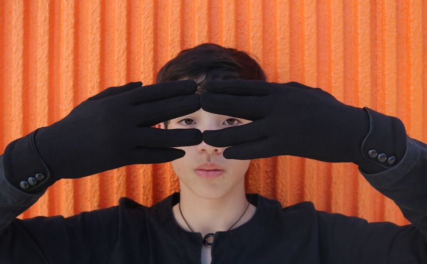 Close-up portrait of boy wearing gloves against orange wall
