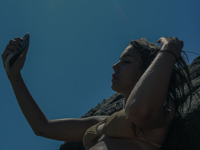 Low angle view of woman photographing against blue sky