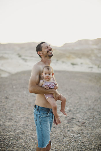A father laughing while holding his baby girl in the desert