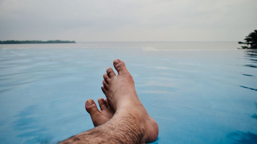 Low section of man relaxing in infinity pool against sea during sunset
