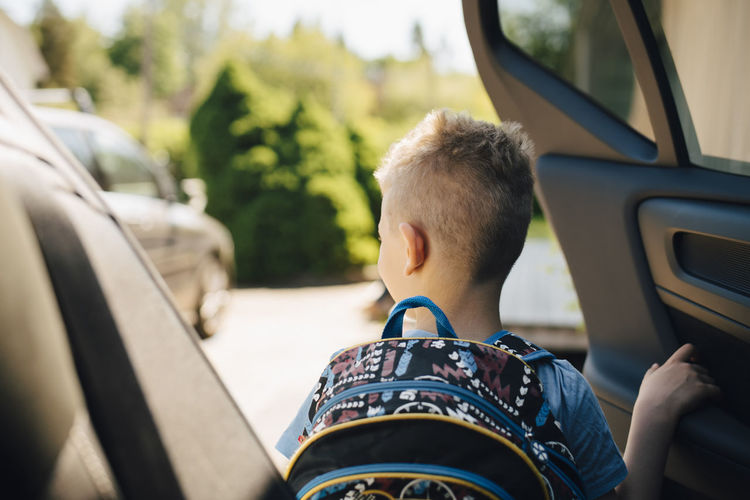 Rear view of boy with backpack opening car during sunny day
