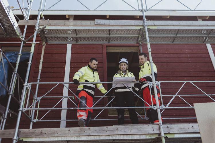 Female building contractor discussing over floor plan with male colleagues at scaffolding