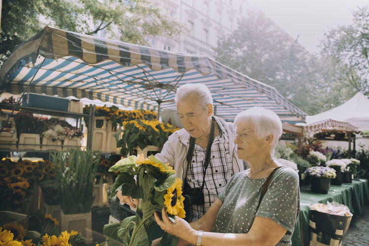 Elderly woman holding sunflowers while shopping with man at flower market in city