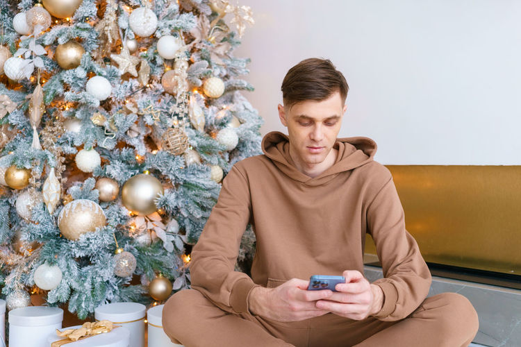 A man sitting on floor near christmas tree orders online goods on black friday