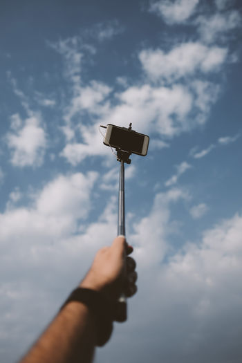 Close-up of hand holding monopod against sky