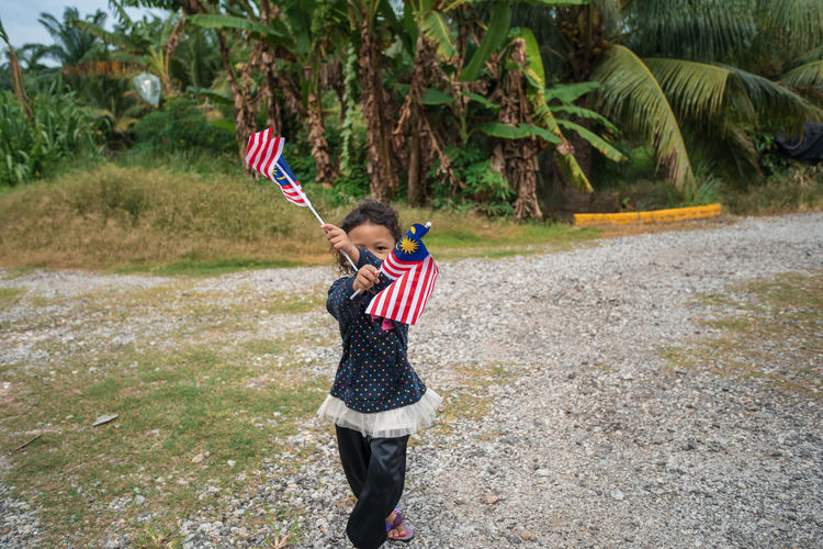 Portrait of girl holding malaysian flags on field 