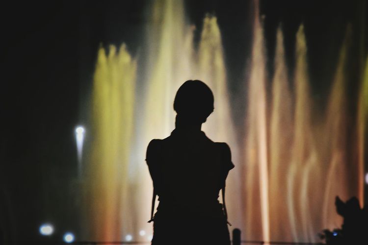 Silhouette woman standing against fountain at night