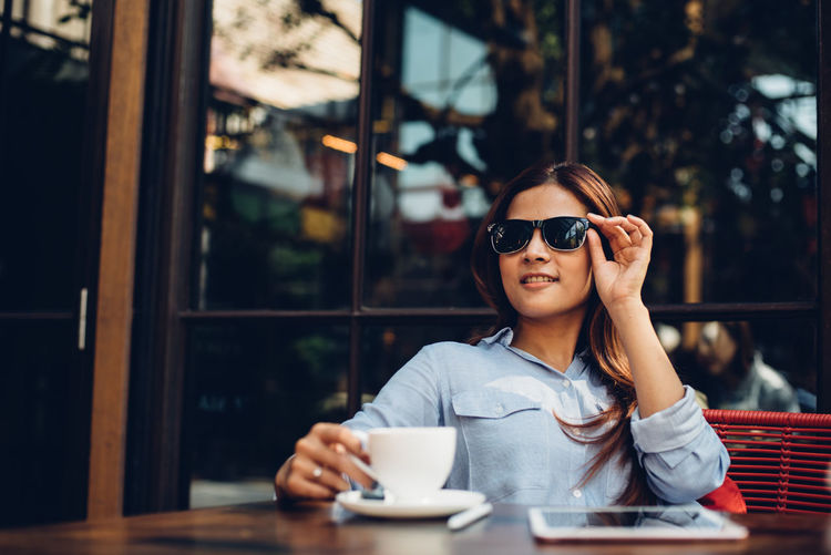 Young woman wearing sunglasses while having coffee at restaurant