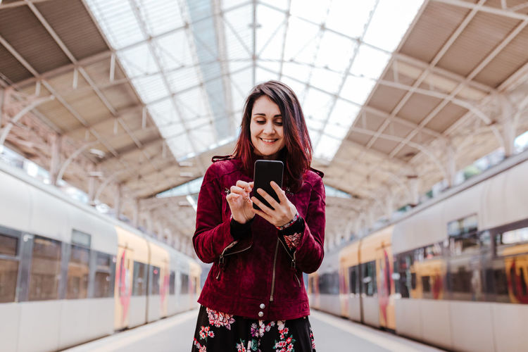 Smiling woman using mobile phone while standing at railroad station platform
