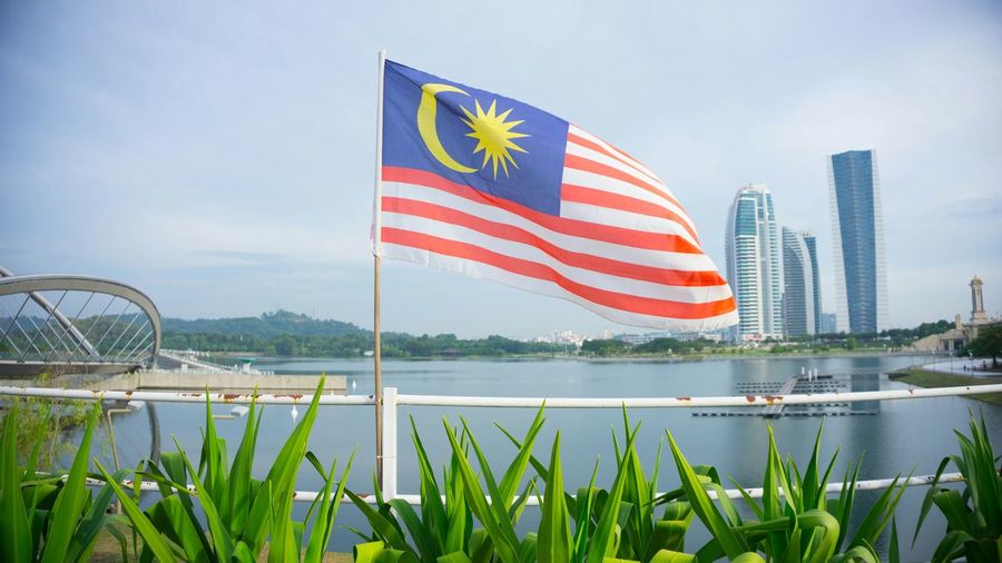 Malaysian flag waving against lake in city