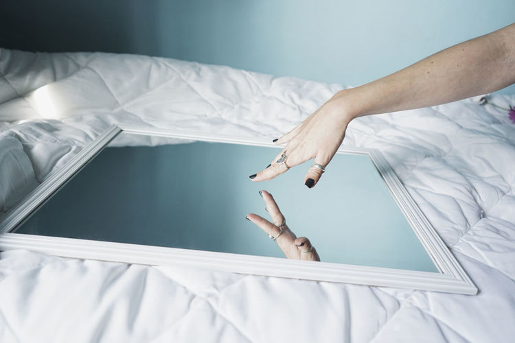 Hand of young woman ltouching mirror lying on white duvet