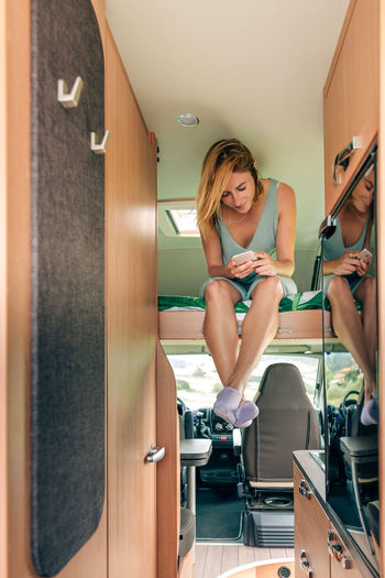 Woman looking cellphone sitting on camper van bunk bed