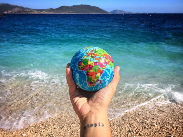 Cropped image of hand holding globe at beach