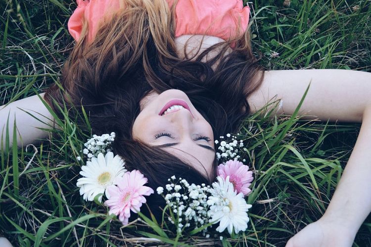 High angle view of smiling woman in flower crown sleeping on grassy field