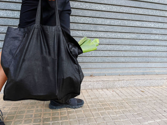 Man carrying black reusable bag with green leek