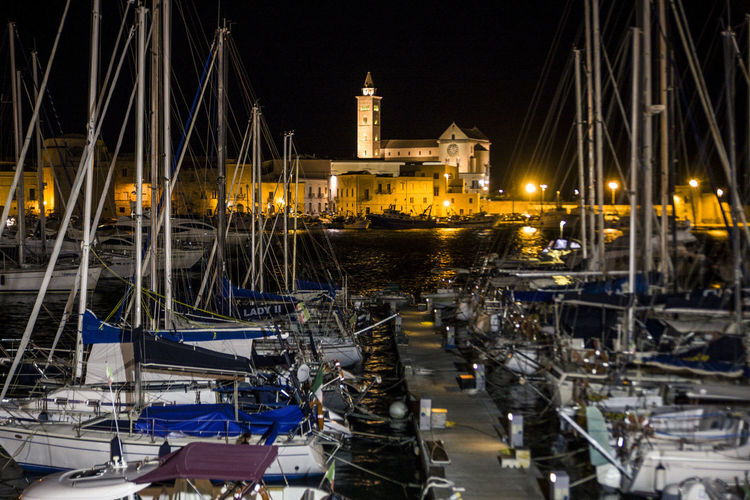 Sailboats moored in harbor by illuminated church against clear sky at night