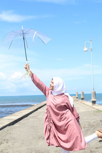 Woman holding umbrella by sea on walkway