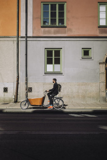 Businessman riding cargo bike against building on sunny day