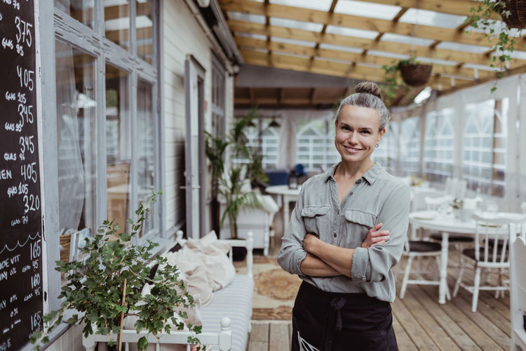 Portrait of smiling businesswoman with arms crossed standing in restaurant