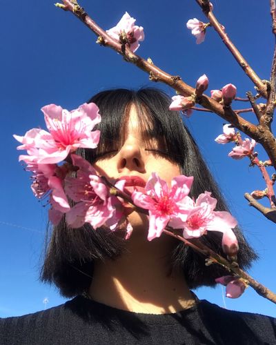 Low angle view of beautiful woman standing with eyes closed near pink flowers against clear blue sky