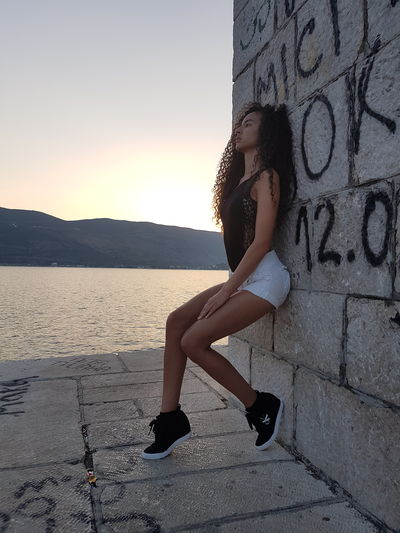 Side view of young fashion model posing on stone wall