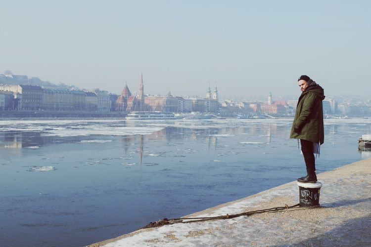 Man standing on bollard by lake in city